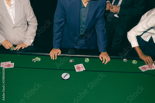 Fotografie Group of professional people sitting around a green felt table playing a high stakes poker card game in a casino setting with chips and dealer button