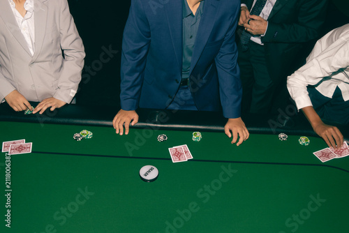 Fotografie Group of professional people sitting around a green felt table playing a high stakes poker card game in a casino setting with chips and dealer button