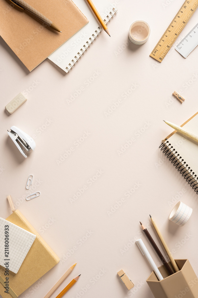 Obraz premium Back to school vertical flat lay with neutral stationery, notebooks and pencils on a pale desk with copyspace in the middle