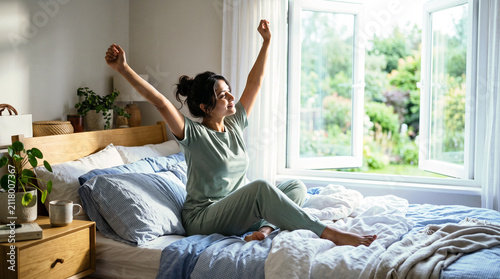 Young woman waking up in bed and stretching her arms in the morning
