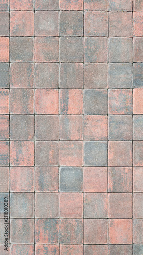 The worn red and gray paving stones are lined with a square pattern. The texture of the street sidewalk with natural color variations