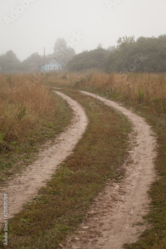 Winding dirt road leading to a village house in autumn morning fog