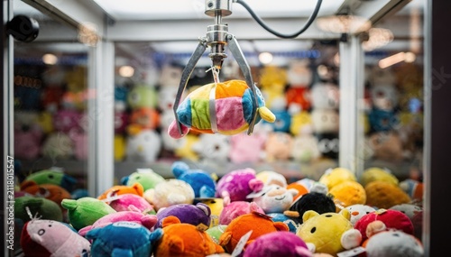 Medium shot of a claw machine stuffed animal wall with a transparent cabinet tightly packed with vibrant plush toys the main claw in focus pulling a prize while the background