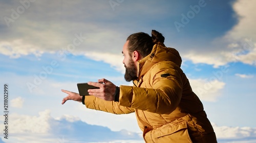 Bild auf Leinwand A reckless adventurer loses balance and drops his phone near a cliff while taking a landscape picture, showing dangerous distraction and careless behavior at high altitude
