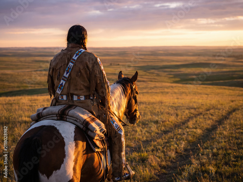 Native American riding horse on prairie at sunset with traditional clothing and peaceful atmosphere