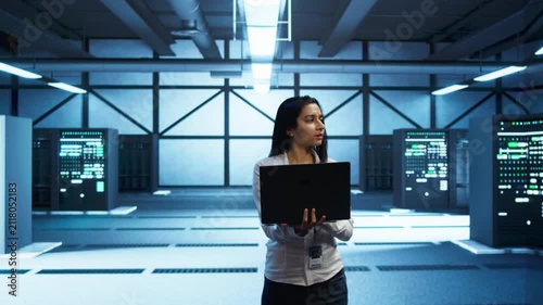 Inside a server hub, iT professional monitors cybersecurity risks with a laptop, linking network security, data protection and performance oversight during hardware and software coordination