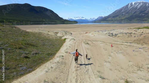 Drone aerial view of woman and dog running on Carcross Benett lake beach in Yukon, Canada