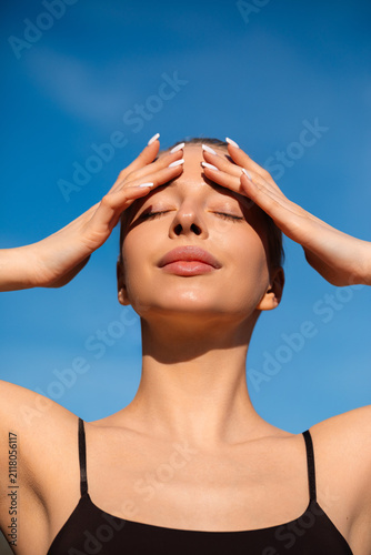 Attractive woman covering forehead from bright summer sunshine. Beauty woman displaying radiant complexion with healthy skin. Sun care concept.