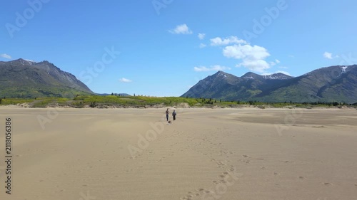 Drone aerial view of couple and dog walking on Carcross Bennett lake beach in Yukon, Canada