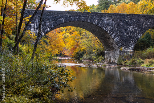 arched stone bridge over a mountain river in the fall