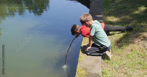 Two kids trying to catch fish with an improvised wood rod with plastic bag attached, in a lake