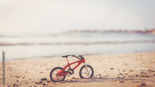Miniature red bicycle on sand of sea beach as a concept of green travel and eco tourism