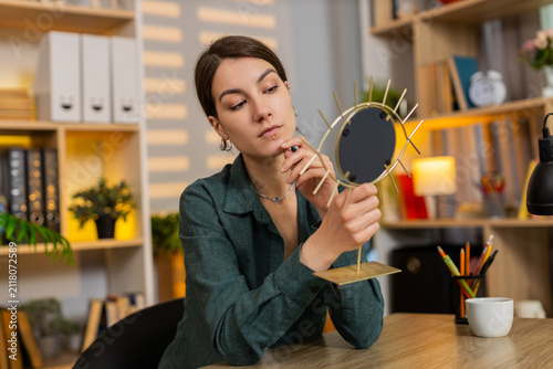 Obraz na płótnie Young woman on home table enjoys mirror reflection smiles with joy during beauty self care break
