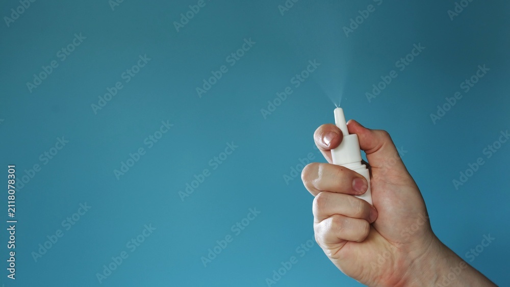 Naklejka premium Hand holding a white nasal spray bottle and spraying mist against a blue background