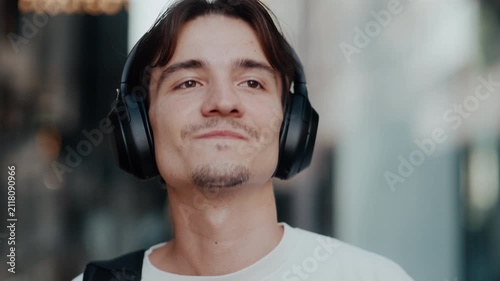 Young man listening to music with black over-ear headphones outdoors