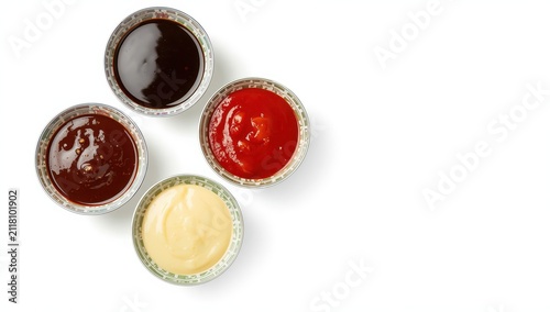 An assortment of vibrant dipping sauces in decorative ceramic bowls, featuring soy, chili, ketchup, and creamy options. Captured from above with bright lighting on a white backdrop.
