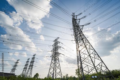 Cuadro en lienzo Multiple high-voltage transmission towers stand under a blue sky with white clouds, supporting power lines