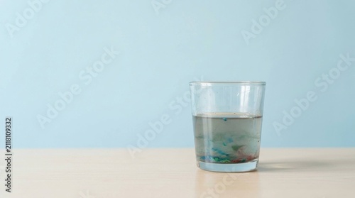 Glass of water with colorful ink settling on a light wooden table background