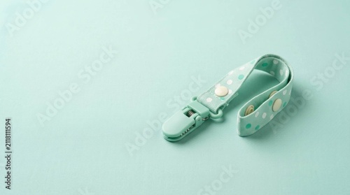 Mint green pacifier clip with polka dot pattern on a matching pastel background