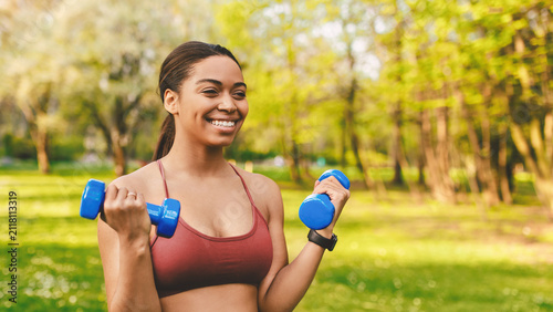 Cuadro en lienzo Smiling Young Black Woman Lifting Dumbbells While Exercising In Park, Enjoying Outdoor Fitness Activities