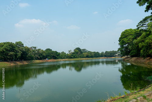 фотографія Tranquil green lake reflecting the surrounding trees under a blue sky