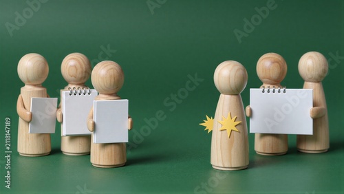Wooden figures hold books, one with a star symbol stands apart.
