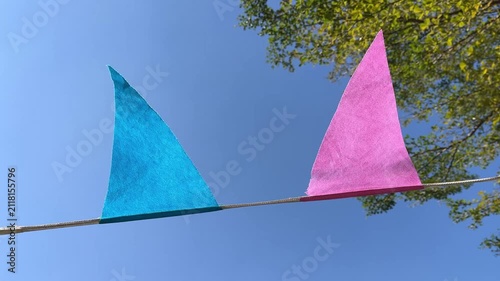 Colorful triangular flags gently flutter in the wind against a clear blue sky, creating a bright, festive, and cheerful outdoor scene filled with movement and summer vibes.