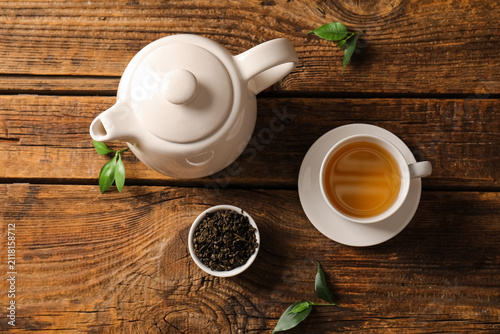 Quadro su tela White ceramic teapot with a cup of hot green tea and loose tea leaves on a rusti