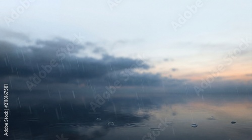 calm water surface with raindrops and dark clouds at sunset