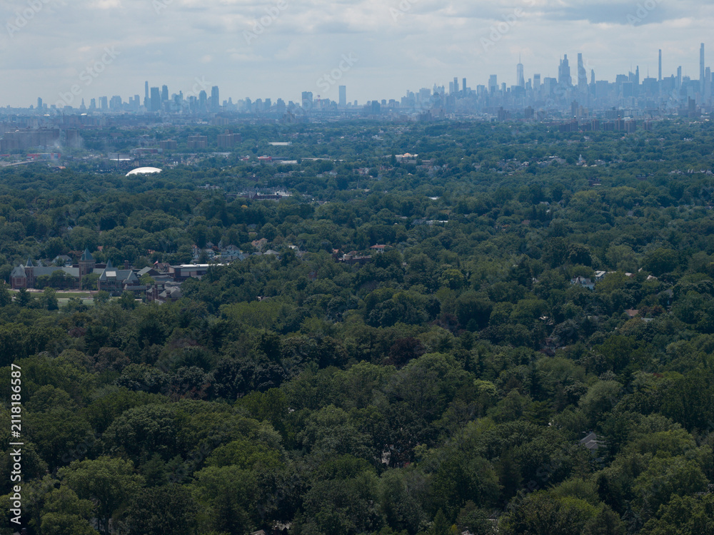 Fototapeta premium Aerial drone view of distant city skyline beyond a wooded suburban landscape in Bayberry Park, New Rochelle, New York