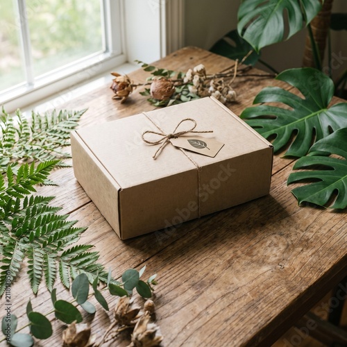 Eco friendly cardboard gift box with leaf tag on rustic wooden table near window