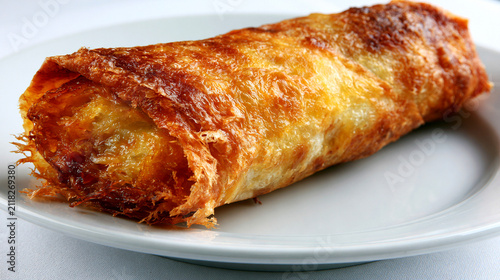 A Single Crispy Fried Spring Roll Centered on a White Plate