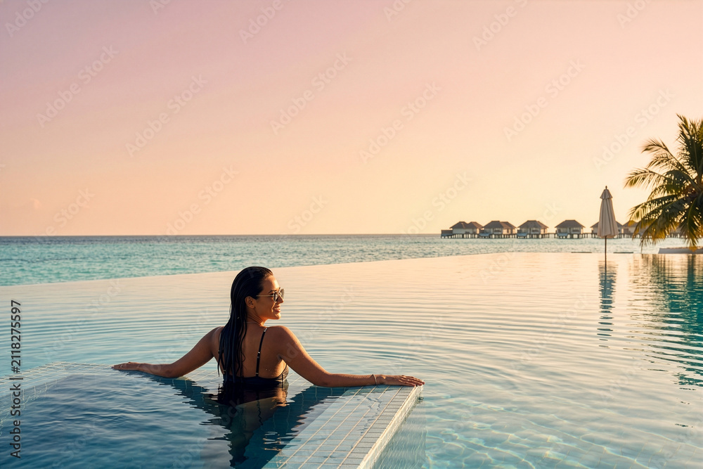 Obraz premium Woman relaxing in infinity pool at tropical resort during sunset