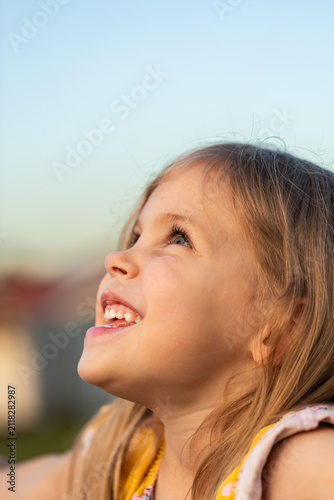 Close up portrait of small child looking up at sunset sky with joy and big smile
