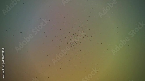 Abstract motion of multicolored tiny particles clustering over a shifting green and yellow gradient background.