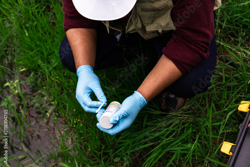 Scientist wearing blue gloves testing water pH level with indicator strip in green farm
