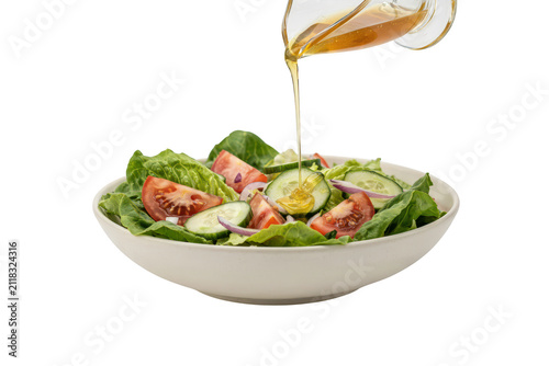 Fresh garden salad in a white bowl with vinaigrette dressing being poured from a glass pitcher isolated on a solid black background view
