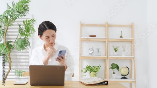 スマホとノートPCを見ながら悩むミドル女性。アプリ、疑問、考える、不安、心配、不満、SNS、家計
