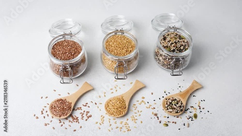 Assortment of seeds in glass jars and wooden spoons on a white background