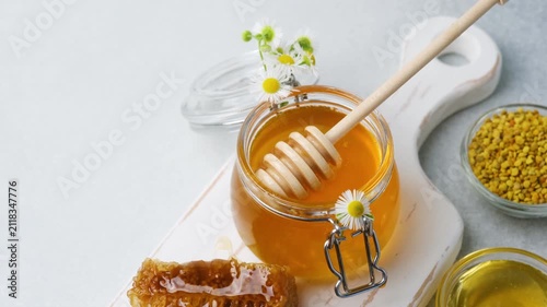 Jar of honey with a wooden dipper and honeycomb on a white board