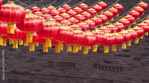 Rows of vibrant red Chinese lanterns hanging against an ancient brick wall background.
