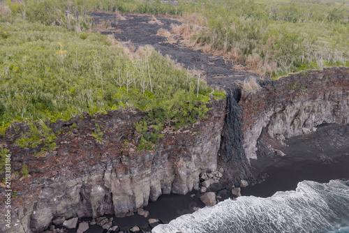 Canvas Print Aerial drone view of dried lava flow cascading over ocean cliff into black sand beach, Piton de la Fournaise volcano, Reunion Island