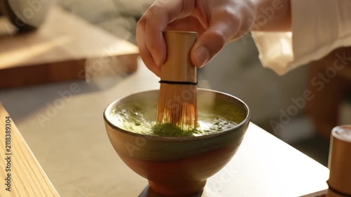 Hand whisking traditional green matcha tea in ceramic bowl