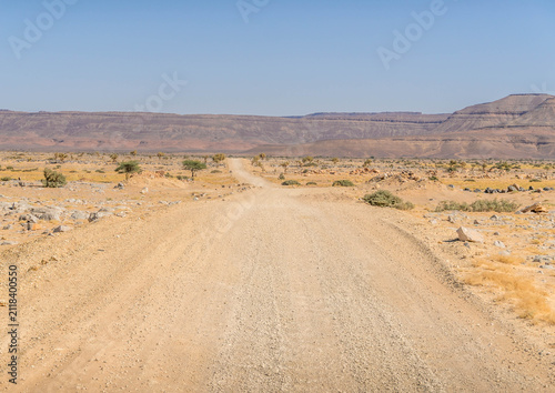 Desert road in Adrar Plateau, West Africa, in Mauritania landscape with sandstone rocks in the horizon, nearby Atar.
