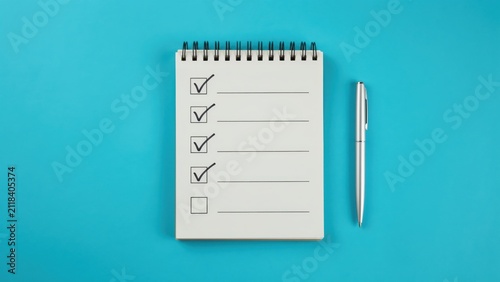 Open spiral notebook with checklist and pen on blue background