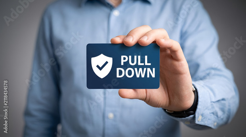 A person in a light blue dress shirt holds a dark blue card displaying a white shield icon with a checkmark and the words PULL DOWN in white text featuring businessman, man, hand and holding