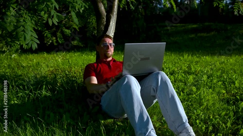 Handsome hipster using laptop in park on a summers day.