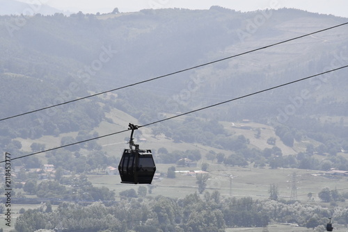 Cable car cabin moving over green mountain landscape on a hazy day