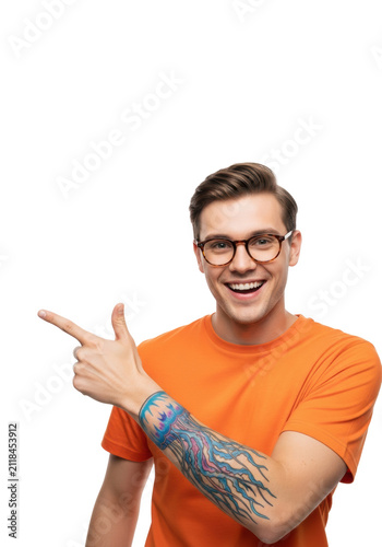 Young caucasian man wearing orange t-shirt and glasses energetically pointing, showing a blue jellyfish tattoo, on bright high-key white studio background. Concept for commercial promotion