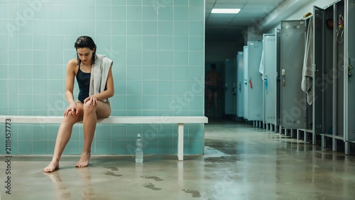 Young woman sitting on bench in locker room, preparing for workout or swim